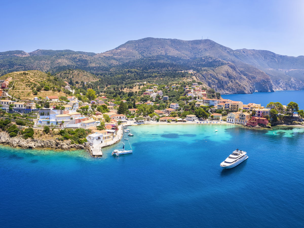 Luftaufnahme einer griechischen Insel mit Häusern auf dem Festland und Booten im Wasser.