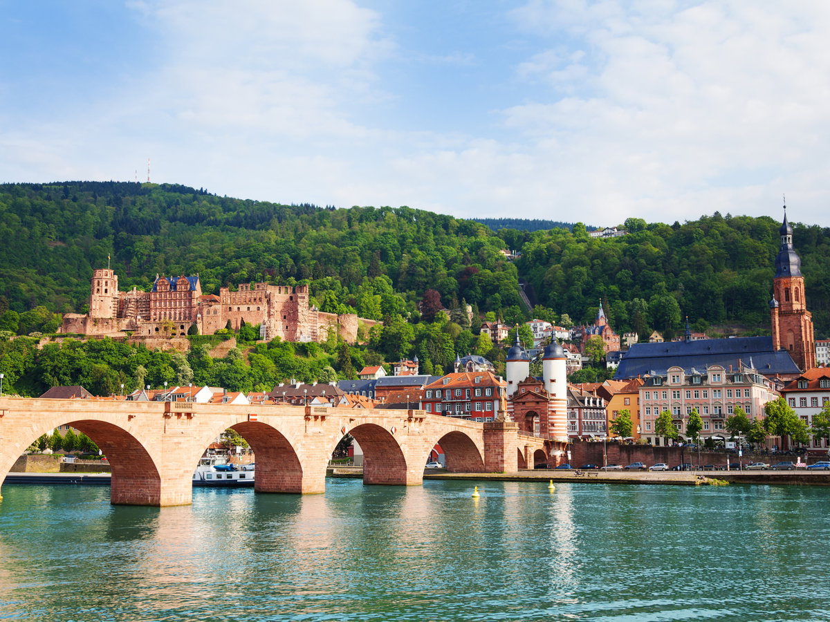 Eine Brücke im Wasser mit Häusern, Burgen und Wäldern im Hintergrund.