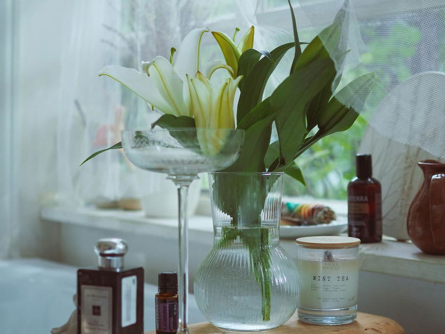 Eine Vase mit Lilien steht auf einem Brett, das über der Badewanne liegt, daneben eine Kerze und ein Parfum.