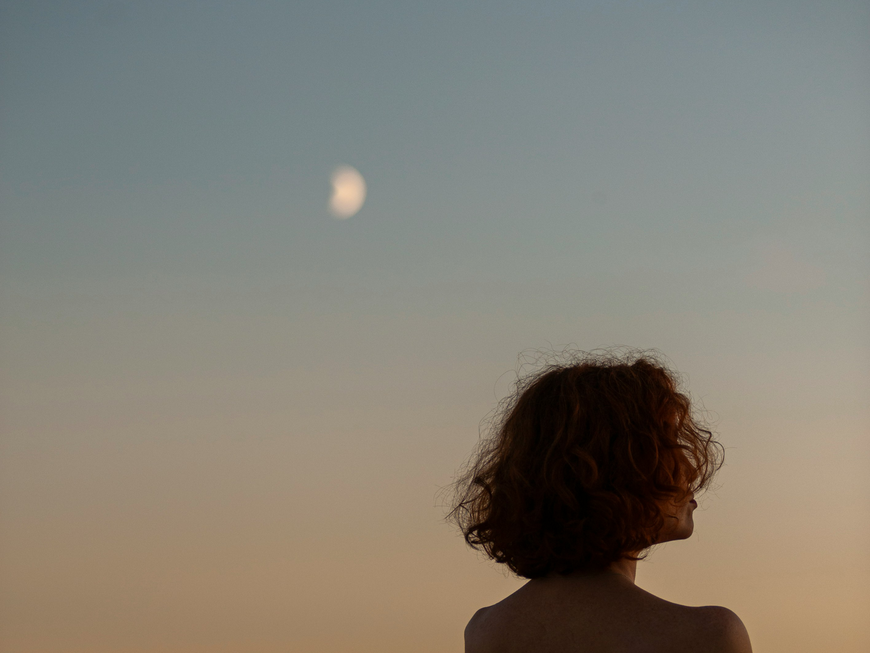 Frau schaut nachdenklich in den Abendhimmel.