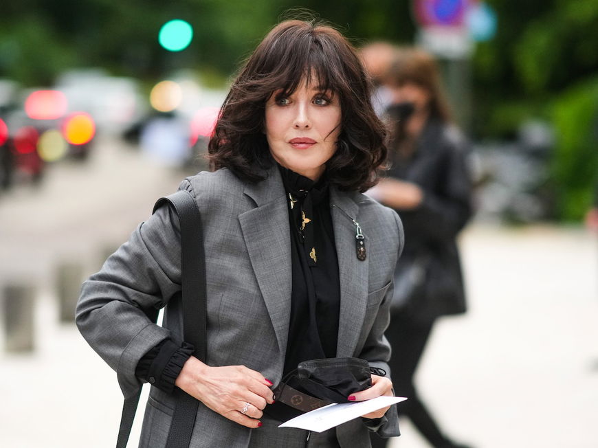 Frau mit dunklem Longbob und Pony trägt eine schwarze Bluse und einen grauen Blazer.