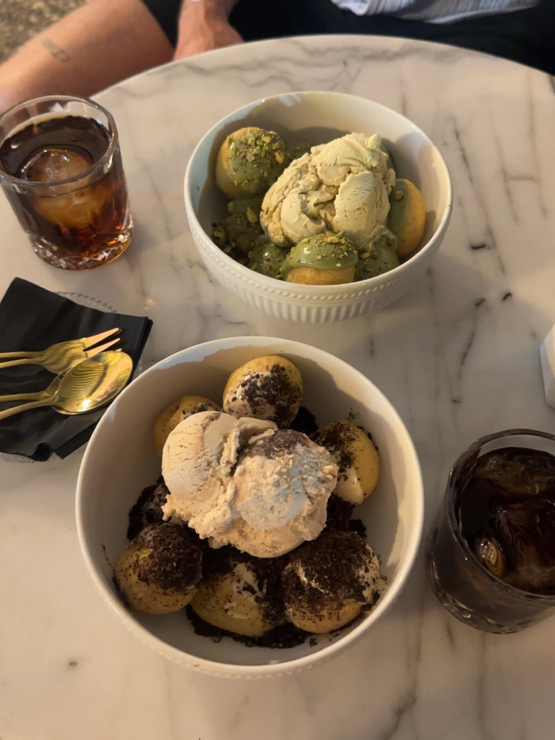 Loukoumades mit Sauce und Eiscreme in zwei Schüsseln auf einem Tisch.