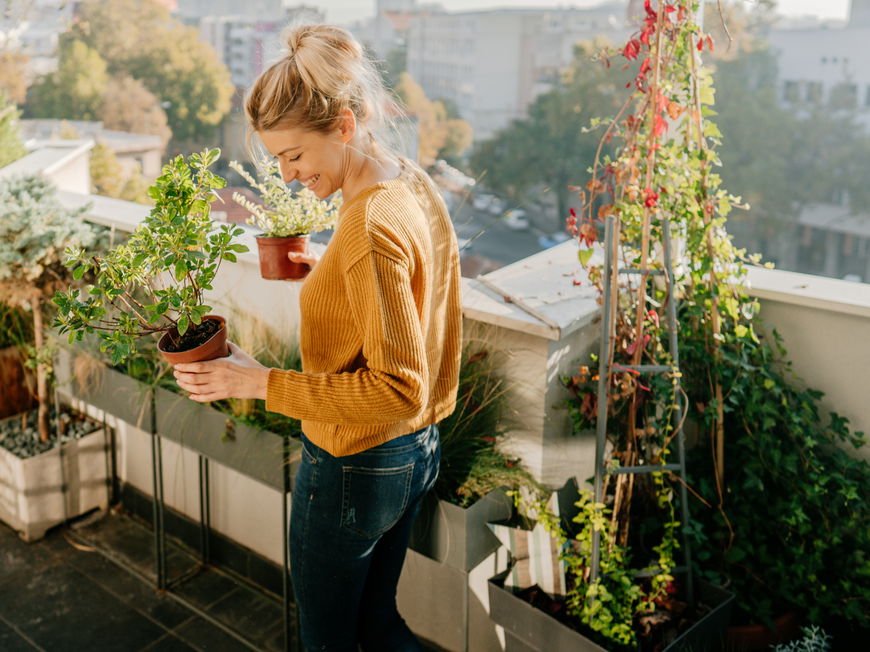 Frau steht auf einem Balkon und hält Pflanzen in der Hand.