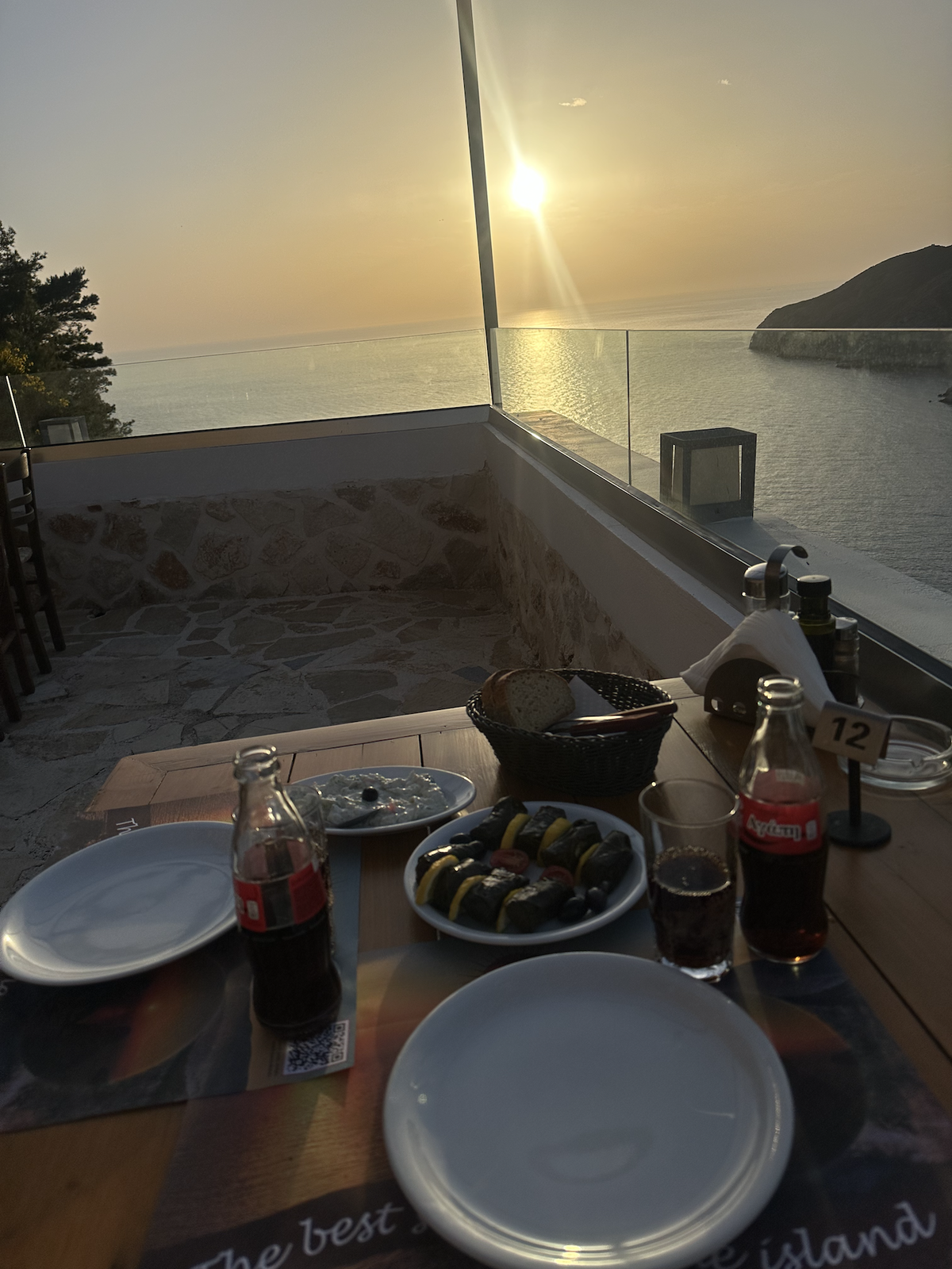 Ein Blick auf einen Tisch mit Essen und Trinken und den Sonnenuntergang über dem Meer im Hintergrund.