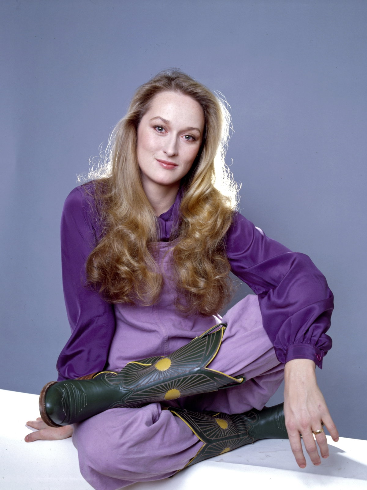 Meryl Streep mit einer lilafarbenen Bluse und Hose sowie Cowboystiefeln und langen blonden Haaren.