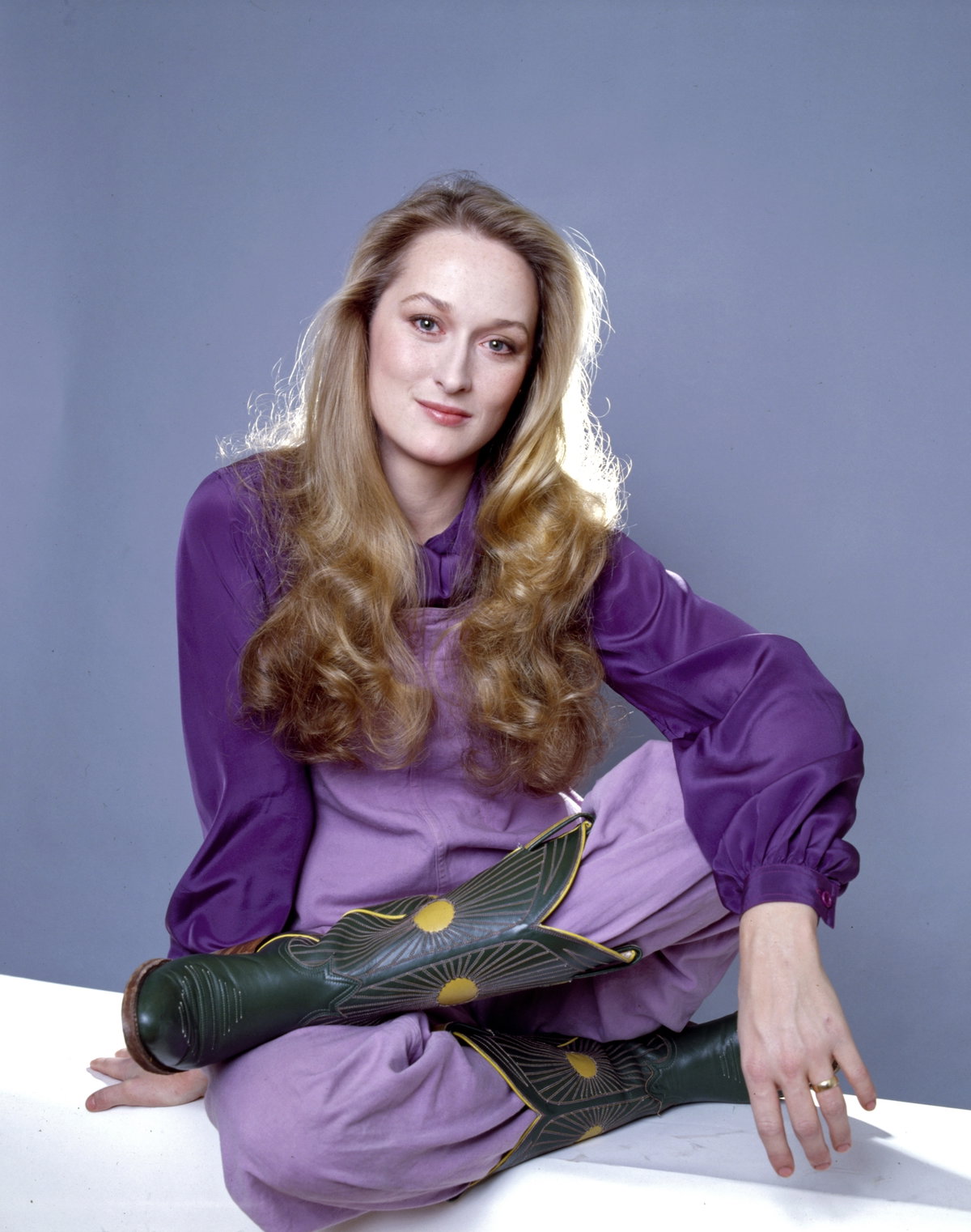 Meryl Streep mit einer lilafarbenen Bluse und Hose sowie Cowboystiefeln und langen blonden Haaren.