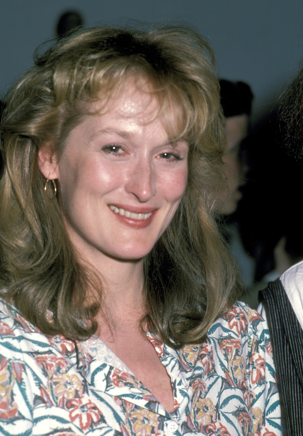 Meryl Streep mit einer Föhnfrisur, kleine Creolen und einem geblümten Oberteil.