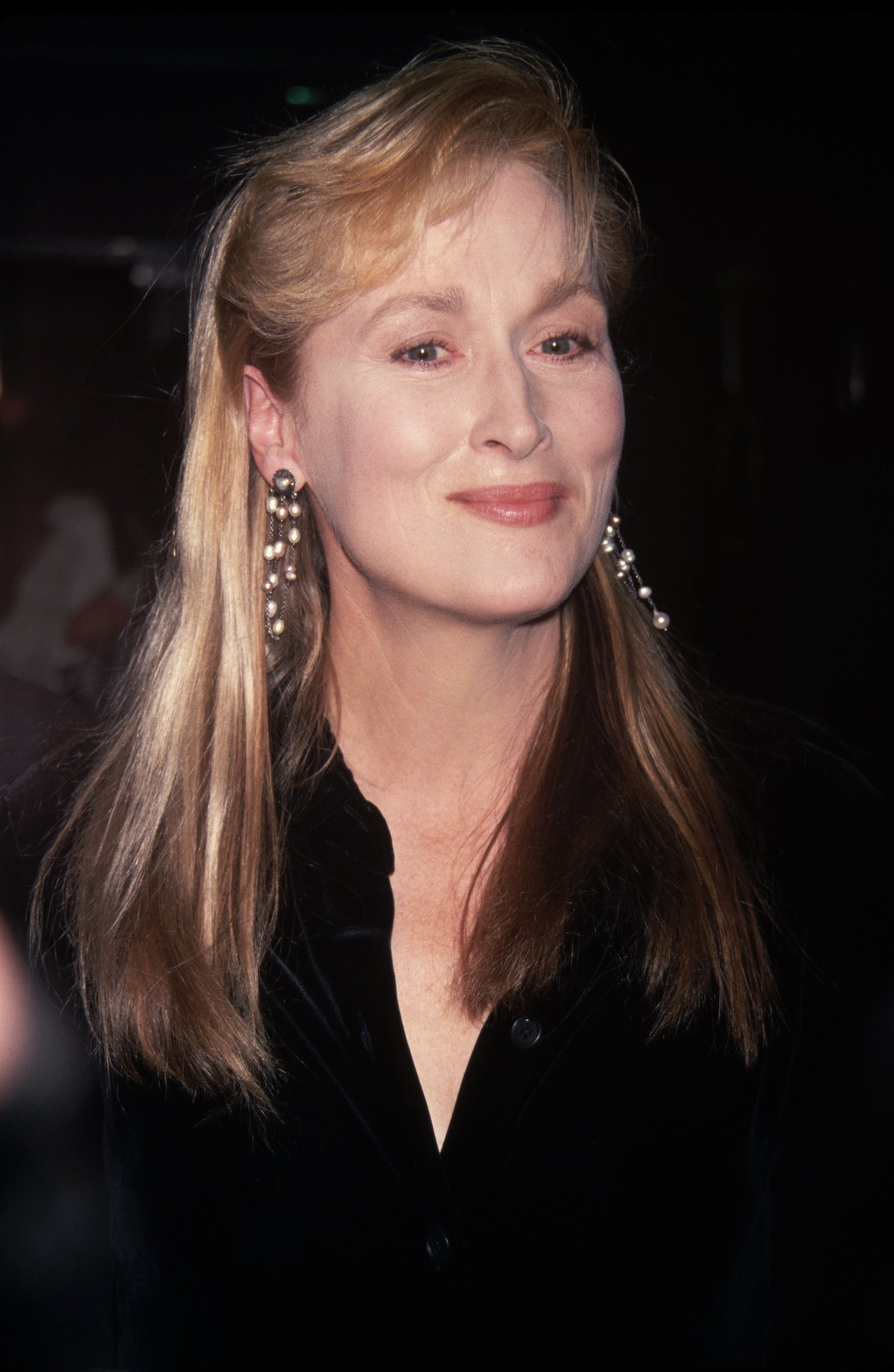 Meryl Streep mit blonden langen Haaren und langen Ohrringen mit Perlen und einer schwarzen Bluse.