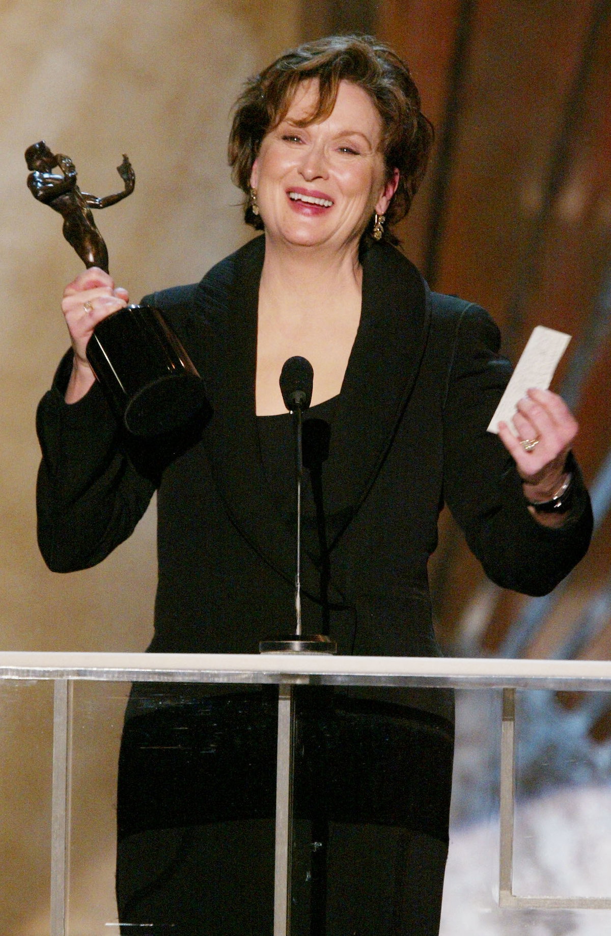Meryl Streep steht mit einer Preisfigur in der Hand an einem Mikrofon.