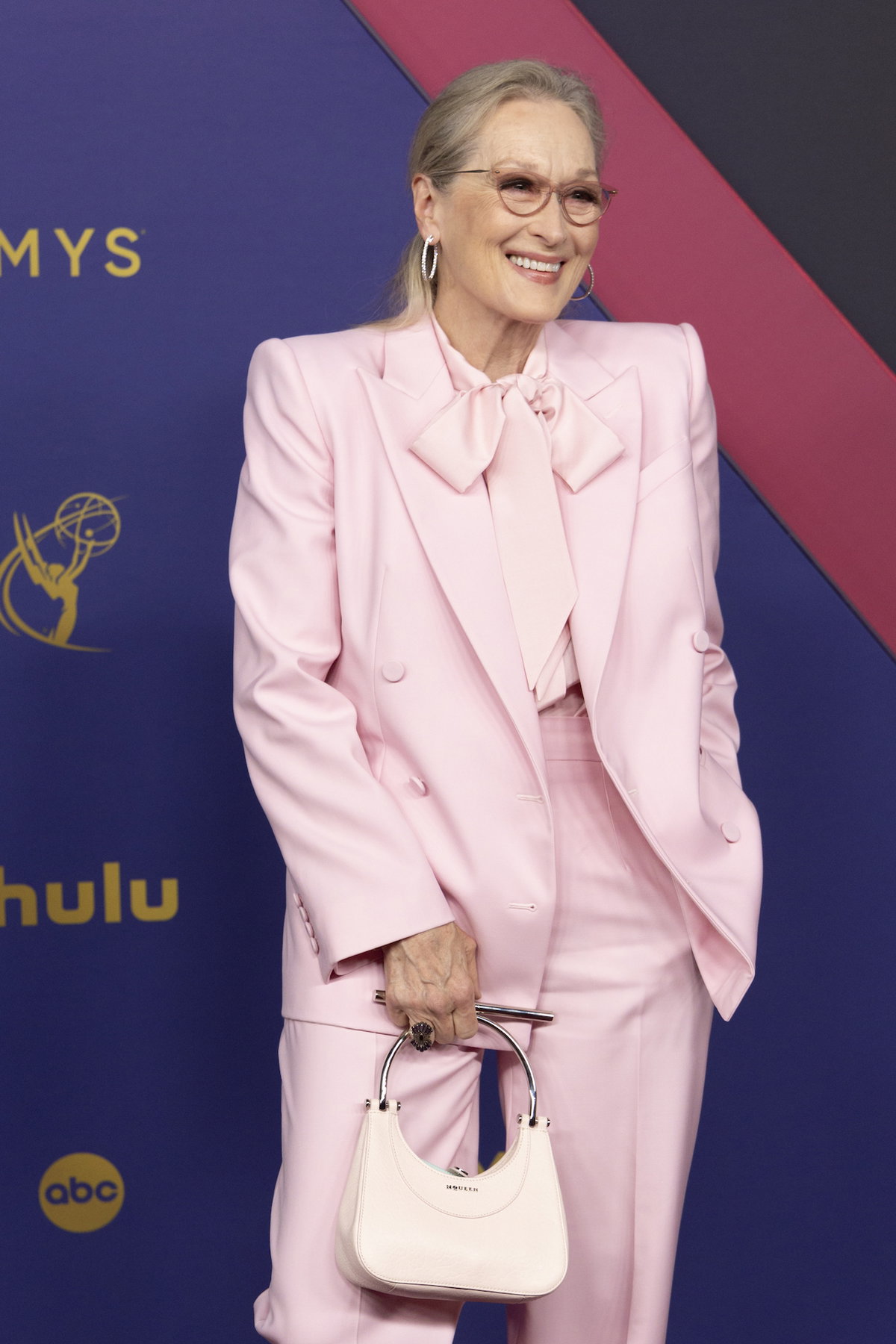 Meryl Streep mit einem rosafarbenen Anzug und einer weißen kleinen Tasche.