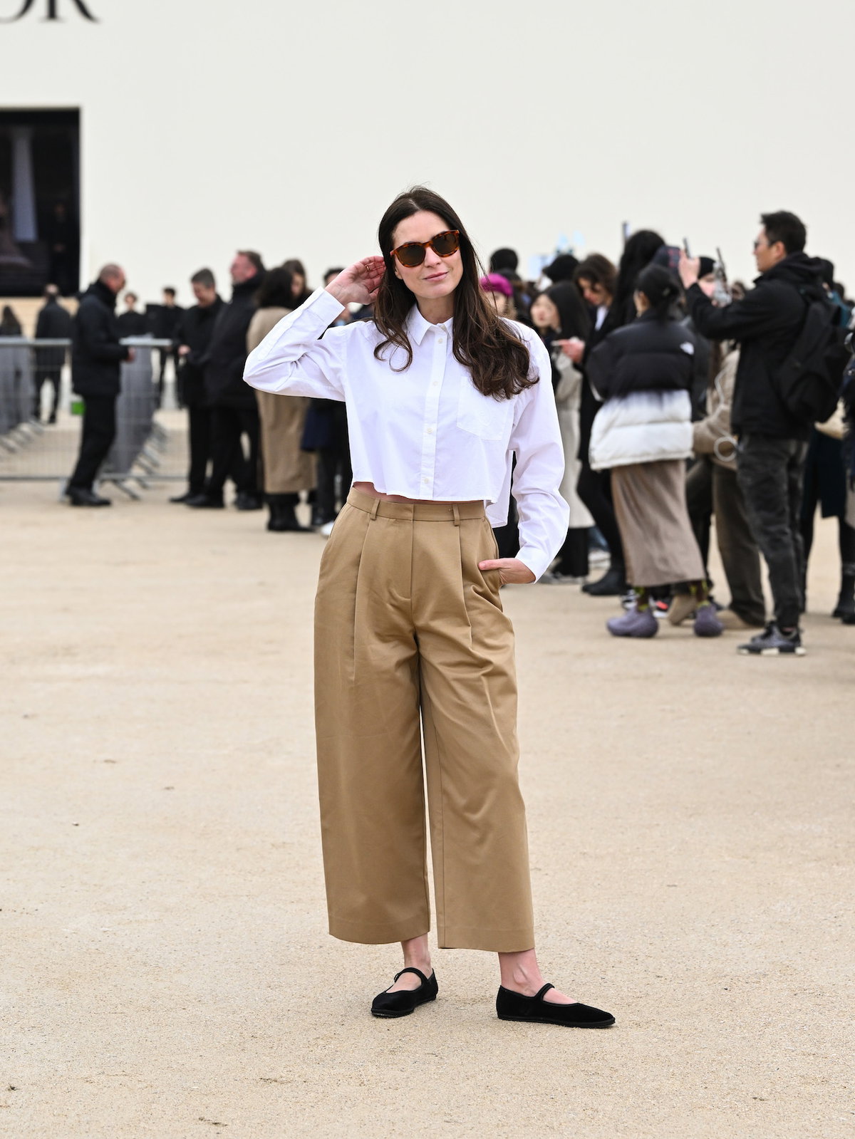 Frau mit braunen Haaren und Sonnenbrille trägt eine weiße kurze Bluse und eine beige Culotte.