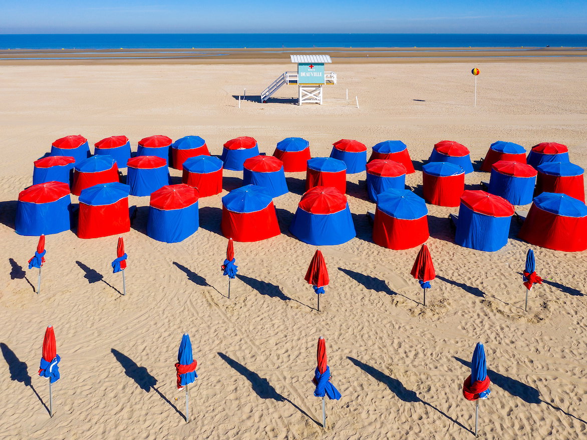 Ein Strand mit vielen blauroten Kabinen und Sonnenschirmen.