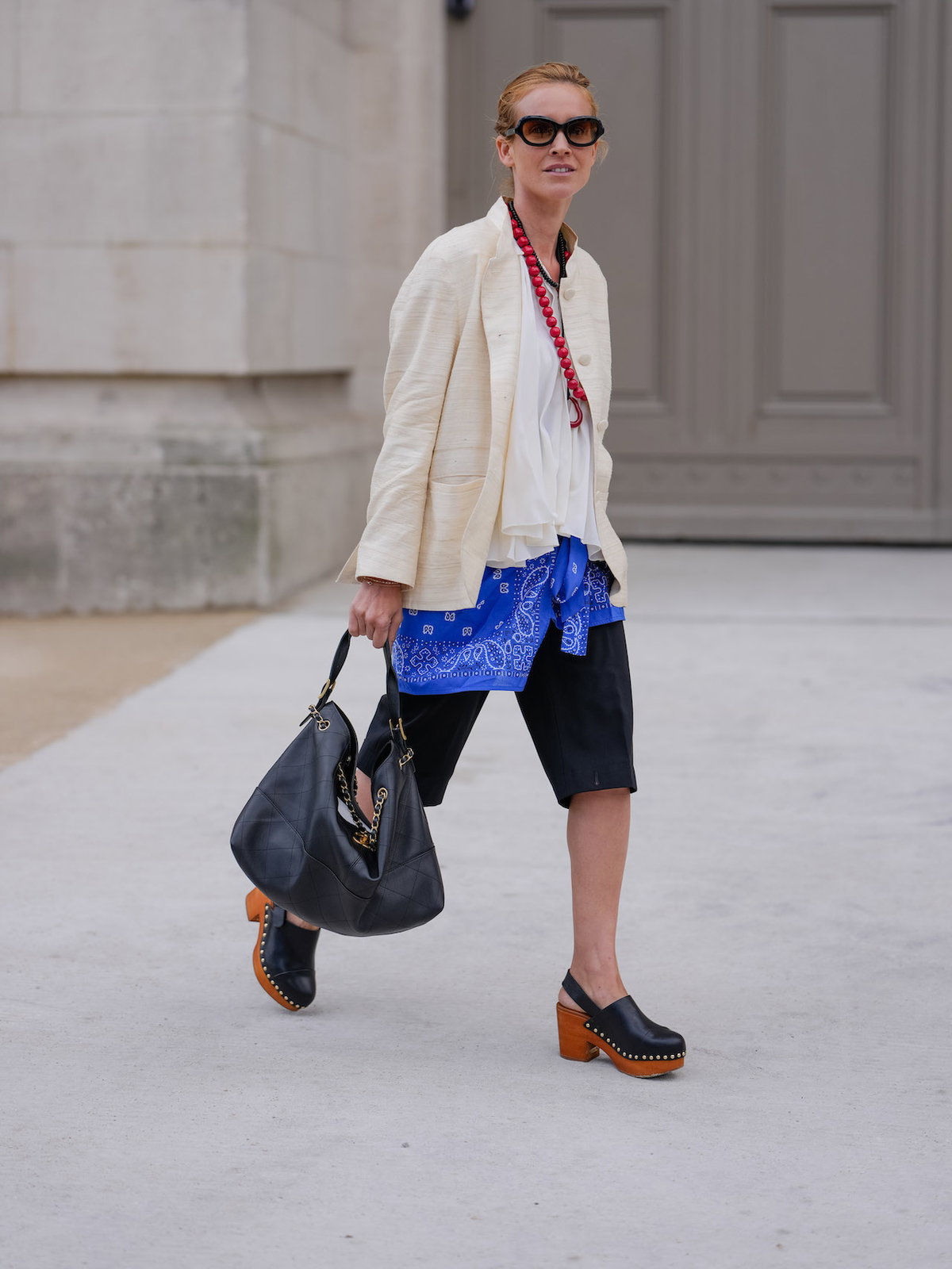 Frau mit beigem Blazer, schwarzen Shorts und Clogs.