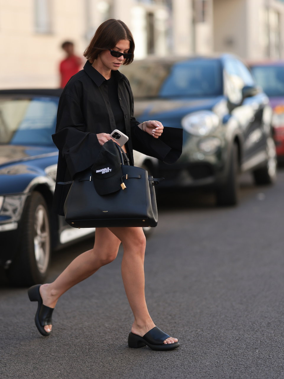 Junge Frau mit braunen Haaren, einer großen Tasche und schwarzen Leder-Sandalen.