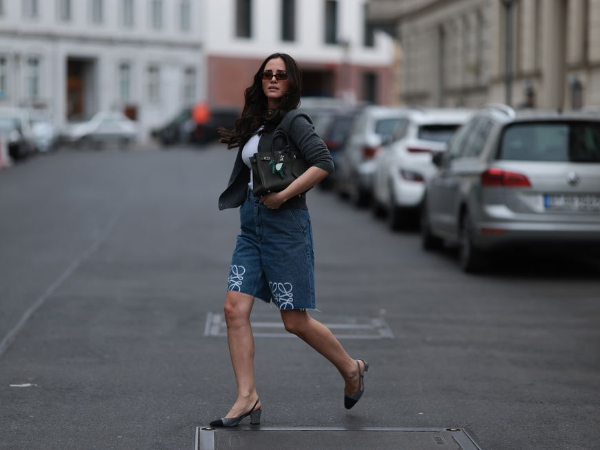 Frau mit dunklen Haaren und Sonnenbrille trägt Jeans-Shorts mit Slingback-Pumps.