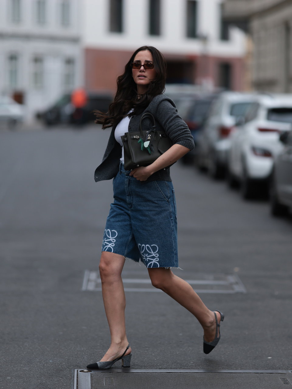 Frau mit dunklen Haaren und Sonnenbrille trägt Jeans-Shorts mit Slingback-Pumps.