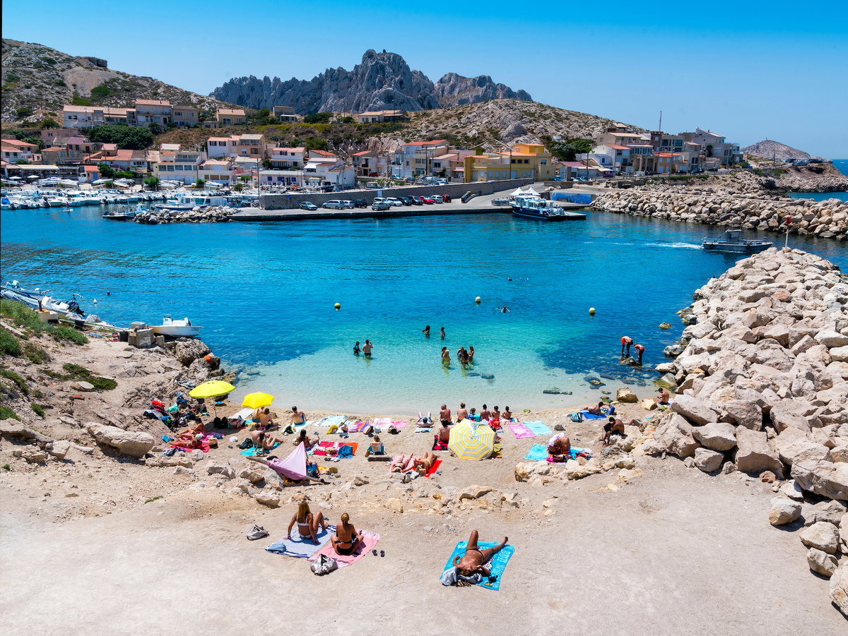Eine kleine Bucht in Marseille mit türkisfarbenem Wasser, Badegästen am Strand und Häusern auf der anderen Seite des Ufers.