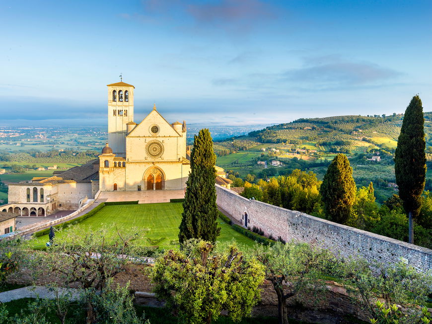 Basilika von Assisi auf einem Hügel mit viel Grünfläche drum herum.