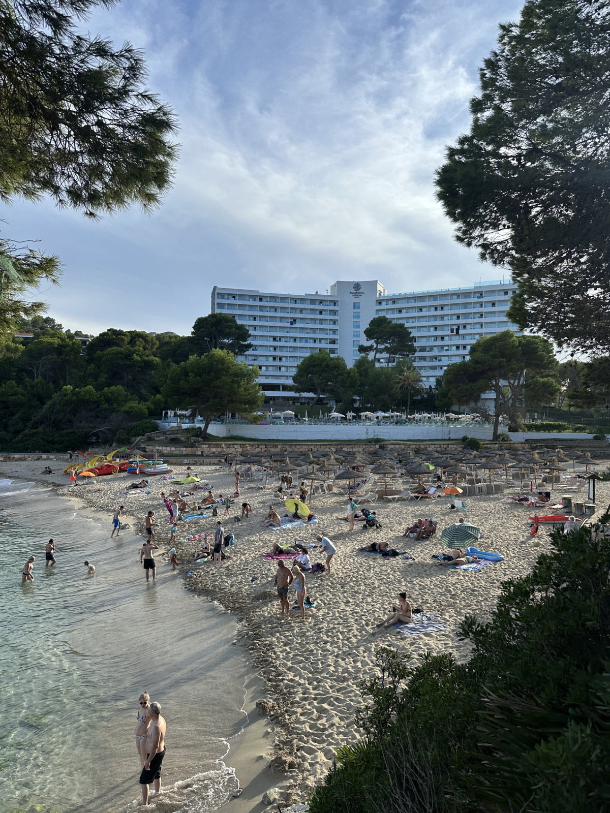 Ein Strand mit Sonnenschirmen, einigen Menschen und einem Hotel im Hintergrund.