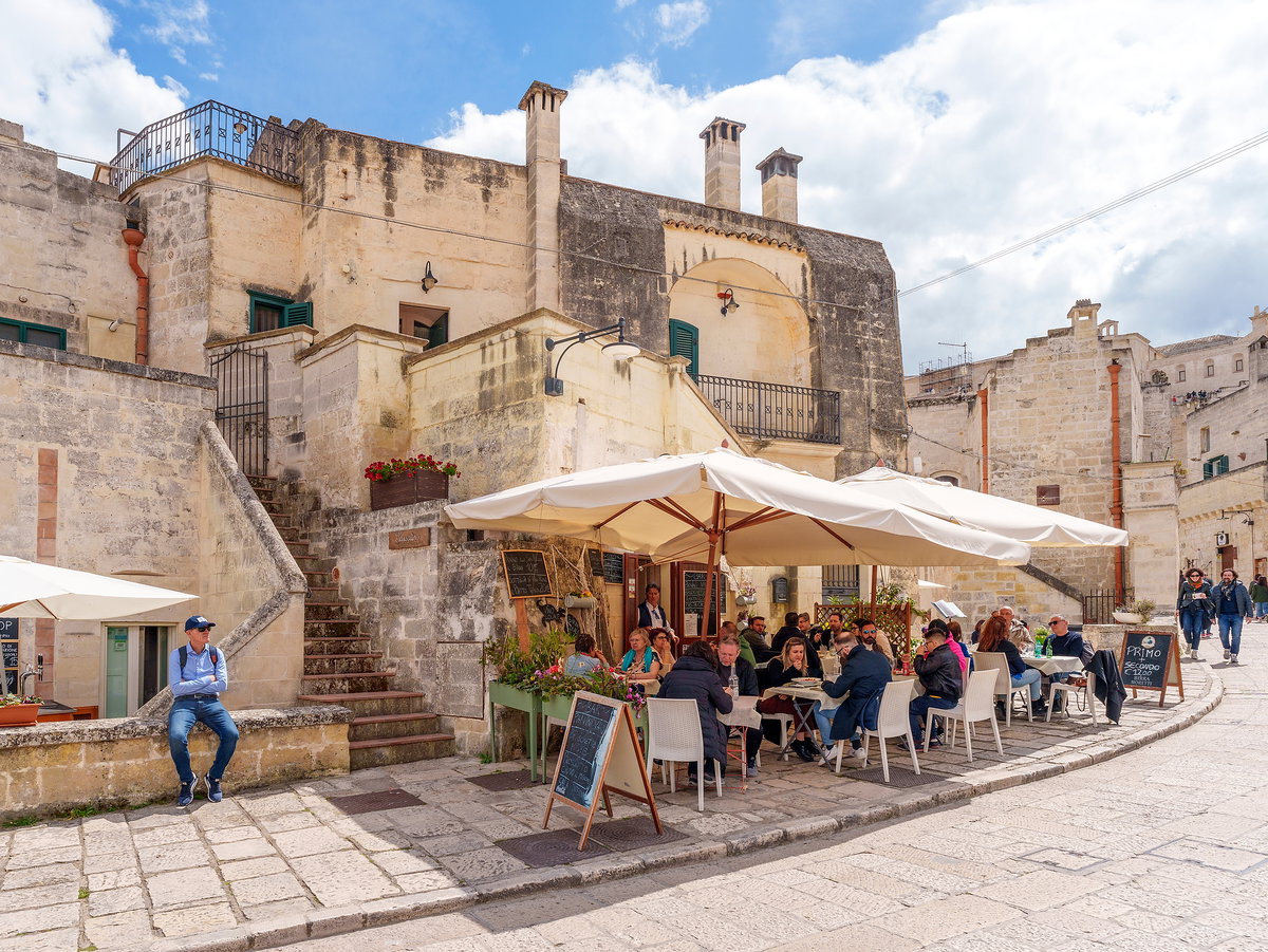 Ein Cafe vor einer Mauer und Burg mit Touristen am Essen.