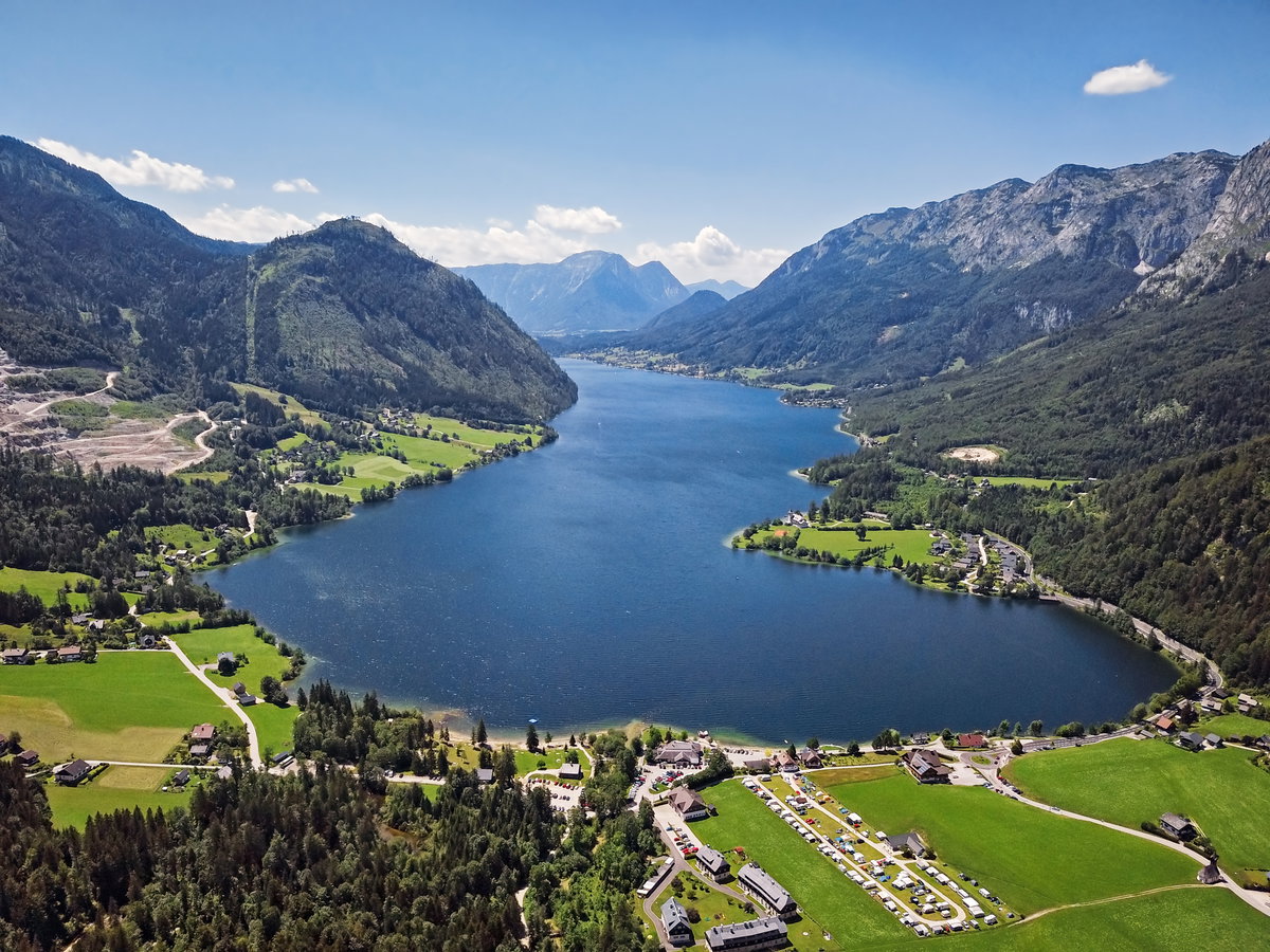Der Grundlsee mit Bergen im Hintergrund, viel Grün und Häusern rund um das Ufer.