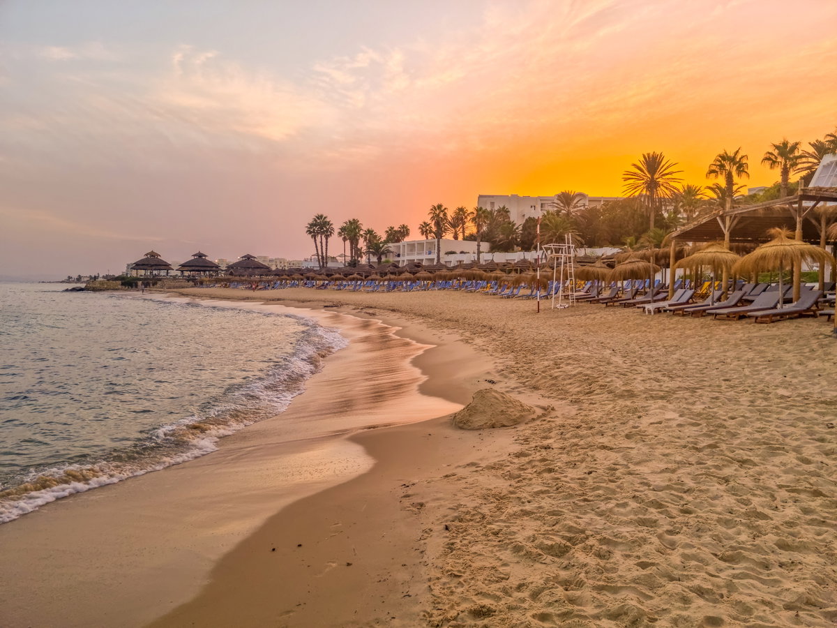 Ein Strand bei Sonnenuntergang in Tunesien mit Liegen und Schirmen.