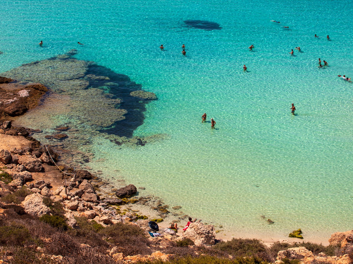 Ein Strand mit Felsen und Menschen im Wasser.
