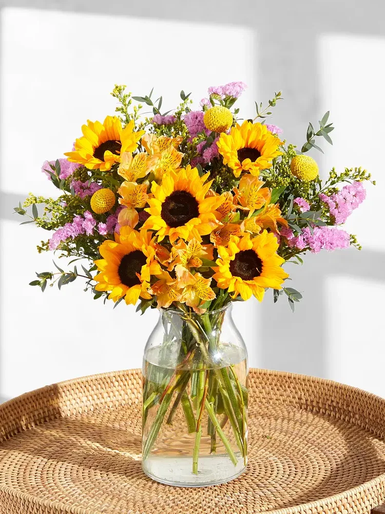 Blumenstrauß mit Sonnenblumen, Inkalilien, Meerlavendel und Eukalyptus auf einem Korbtablett.