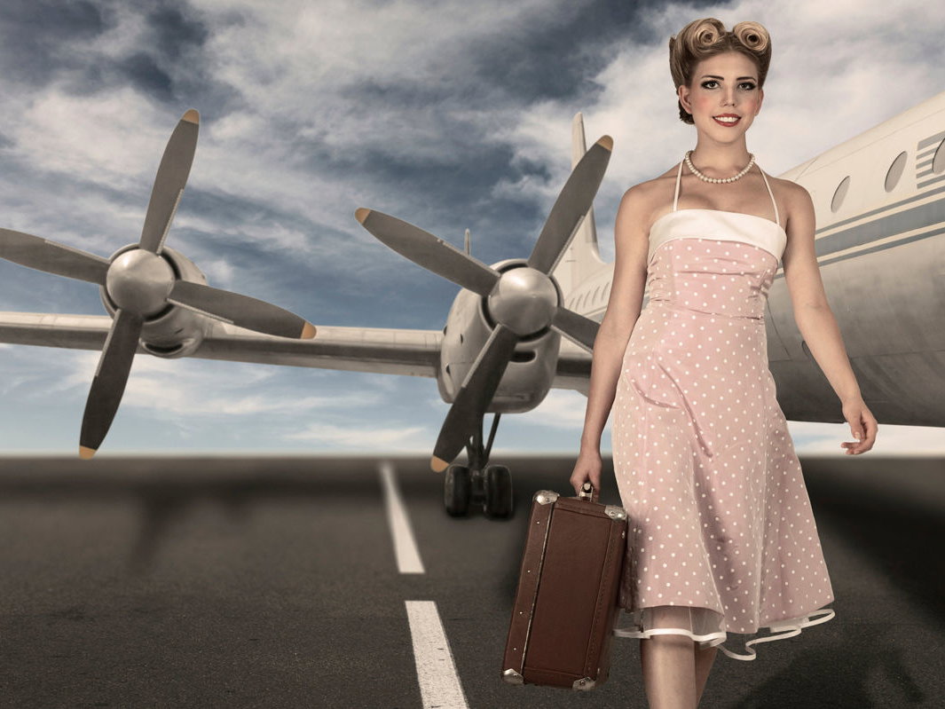 Frau im Sixties-Look mit Koffer vor einem Flugzeug
