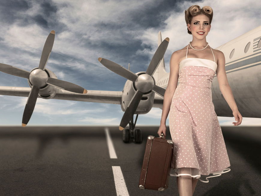 Frau im Sixties-Look mit Koffer vor einem Flugzeug