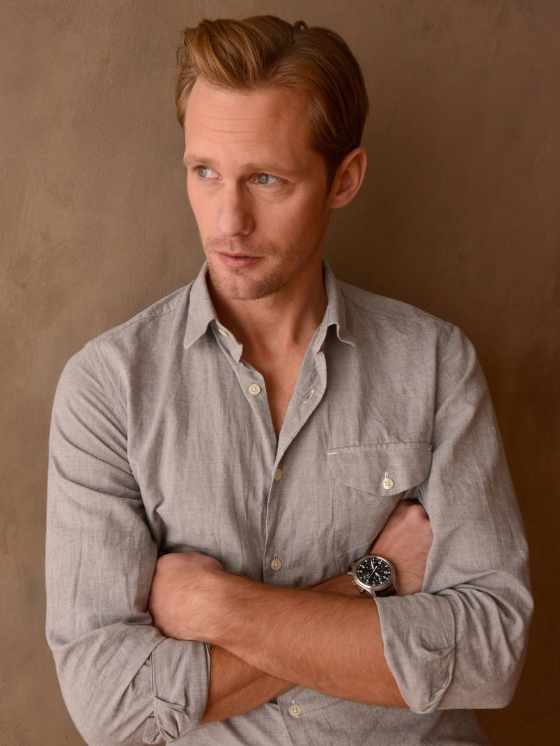 Alexander Skarsgard mit einem hellgrauen Hemd und verschränkten Armen vor der Brust.